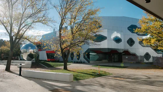 Modern building with geometric patterns and a large reflective spherical sculpture near trees in autumn.