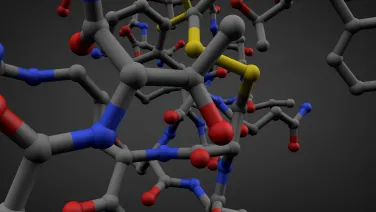 3D molecular model showing a complex arrangement of atoms in various colors including blue, red, yellow, and gray, set against a dark background.
